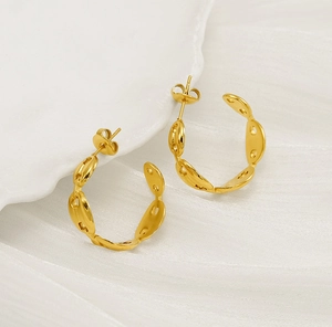 Macro shot of gold-plated pig nose C-shaped earrings on white silk and ceramic plate