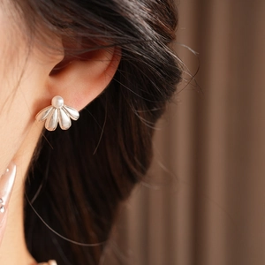 Close-up of silver shell-shaped earring with pearl detail worn on model's ear