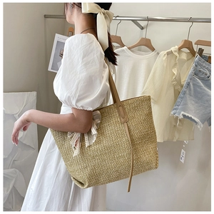 Detail of a beige woven straw tote bag held by a model in a minimalist cream setting
