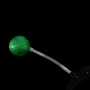Detail of glowing green glitter alien eyeball headband with silver spring on black background