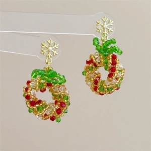 Detailed macro view of handmade beaded Christmas wreath earrings with red bows and gold flakes