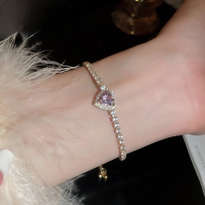 Detail of elegant gold heart bracelet with pink gemstone on female wrist over gift box