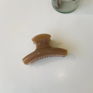 Detail view of a glossy brown resin shark hair claw clip on a plain white background