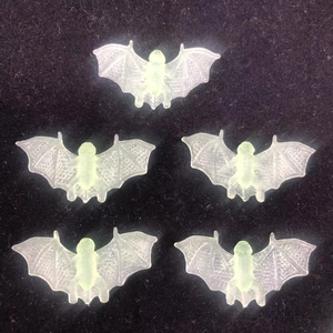 Close-up of five semi-transparent green bat toy accessories on black velvet surface