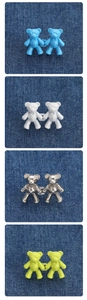 Detail of bear-shaped waist cincher buttons in blue, white, silver, and neon green on denim