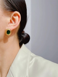 Close-up of vintage gold oval earrings with emerald green stone worn by a model