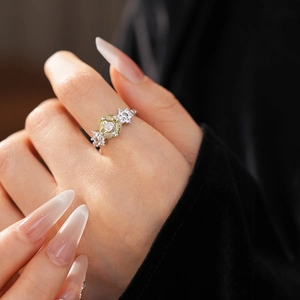 Close-up of a vintage flower ring with an oval yellow-green gemstone on finger