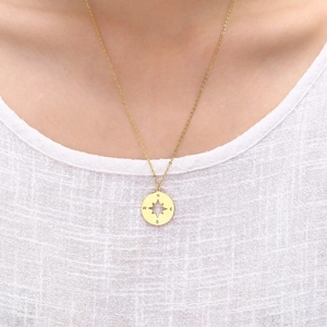 Golden compass necklace detail with engraved coordinates on linen apparel background