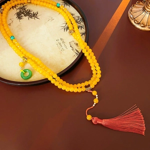 Détail d'un collier à perles jaunes avec pompon rouge et pendentif anneau de jade vert