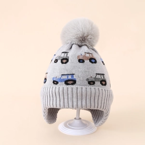 Detail view of winter knitted baby hat with car pattern and soft pompom on a stand