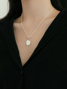 Detail of silver toggle clasp necklace with textured oval coin pendant on model