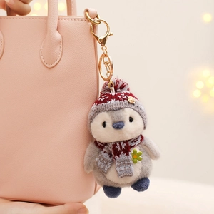 Cute plush penguin keychain with red scarf hanging on a pink bag as accessory
