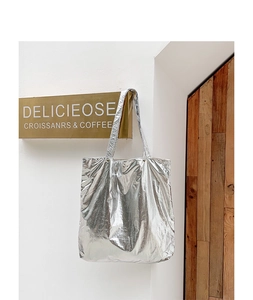 Silver metallic tote bag with crinkled texture hanging against a minimalist white wall