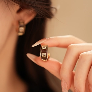 Detailed close-up of C-shaped gold-plated earring with brown enamel and square gemstone