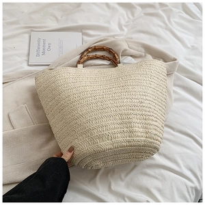 Detailed view of beige straw tote bag with bamboo handle on soft white fabric background