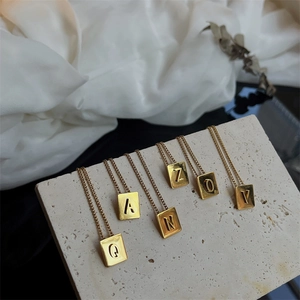 Detailed close-up of golden square letter pendants on textured stone and white silk fabric