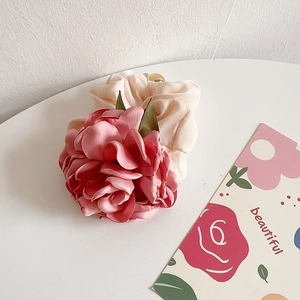 Detail of pink floral fabric scrunchie with green leaves on a minimalist white surface
