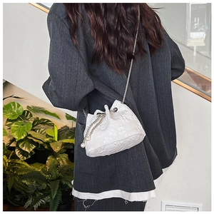 Close-up of a white jacquard drawstring bucket bag with chain strap and pearl charm details