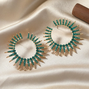 Exaggerated golden flower earrings with green rhinestones on silk background