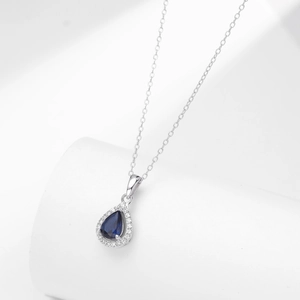 Macro view of blue pear-cut zircon pendant with silver halo setting on delicate chain