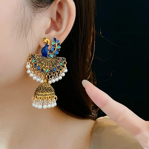 Close-up of golden peacock earrings with blue enamel, pearls, and jhumka tassels