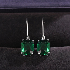 Detailed view of emerald cut green gemstone drop earrings hanging in a black jewelry box