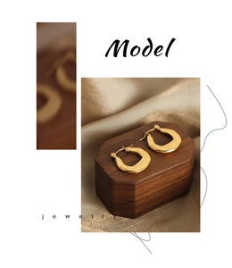 Detailed view of chunky gold U-shaped earrings on a wooden box with satin fabric