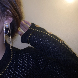 Detail of luxury pearl and rhinestone fringe earrings worn by a model on black knitwear