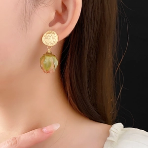 Detailed view of model wearing gold hammered earrings with resin rose bud charms