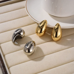 Close-up of gold and silver teardrop stud earrings with polished mirror finish on velvet tray