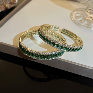 Detail shot of emerald green square stones and pavé crystals on a golden open bangle