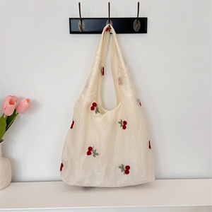 Detail of embroidered cherry patterns on a creamy white tulle tote bag hanging on a hook