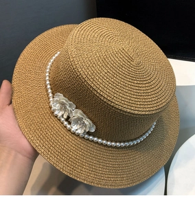 Detail of hand-woven straw hat featuring pearl chain and white floral accents