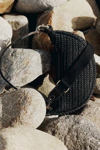 Detail of black woven crescent bag with leather strap and gold hardware on rocks