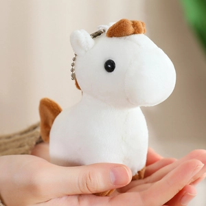 Close-up of a white plush pony keychain held in hand with soft brown mane details