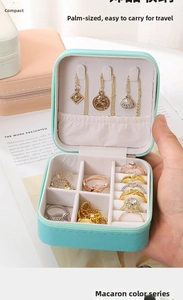 Hand holding a mint green leather travel jewelry box with multiple interior compartments