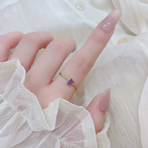 Macro detail of a purple rectangular amethyst ring on a gold textured band with four prongs