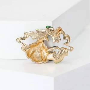Golden ladybug beetle brooch with green enamel details on minimalist white display