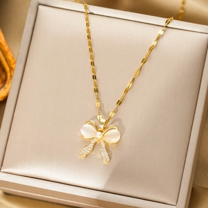 Champagne gold bow necklace featuring white cat-eye stones and pearl accents in a jewelry box