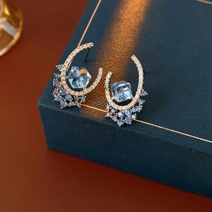 Detail of C-shaped gold earrings with blue hexagonal gems on a luxury jewelry box