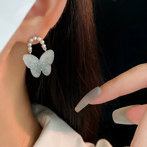 Close-up of asymmetric butterfly earrings with white pearls and blue translucent charms