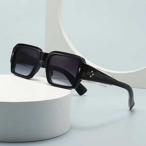 Square black sunglasses with gold metal star accents and gradient lenses on a modern stand