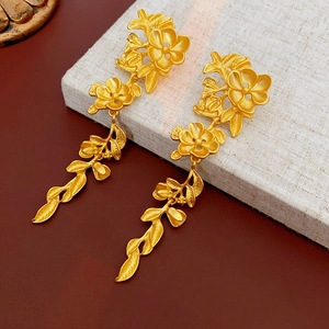 Détail de boucles d'oreilles pendantes à fleurs en or mat sur une boîte cadeau