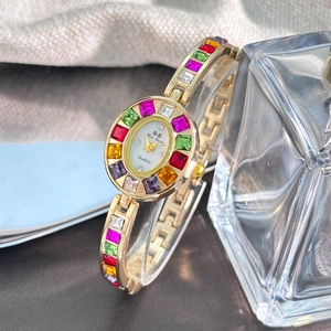 Close-up of golden women's watch with colorful zircon crystals and oval dial on display