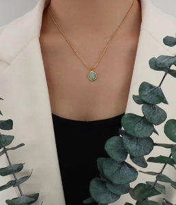 Detail of 18k gold plated necklace with green cat-eye stone worn with a white blazer
