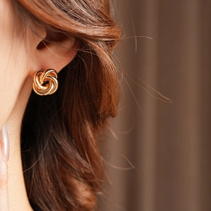 Close-up of golden knot earrings on model ear, showcasing stylish minimalist metal jewelry