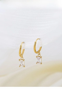 Macro detail of gold hoop earrings with square zircon pendant on white mesh ribbon