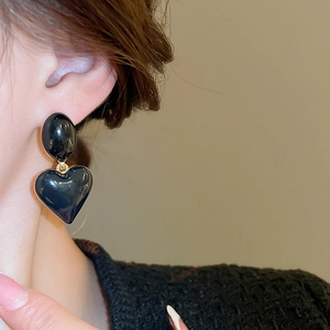 Close-up of elegant black heart-shaped pendant earrings with gold edges on a model