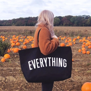 Black canvas tote bag with white Everything print worn by a model in autumn setting