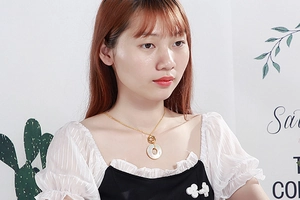 Close-up of a gold stainless steel necklace with a circular white shell pendant on a model